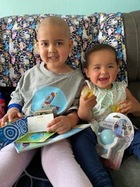 two young girls sitting on a couch with books and toys