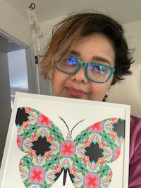 a woman in glasses holding up a butterfly framed in a hospital room